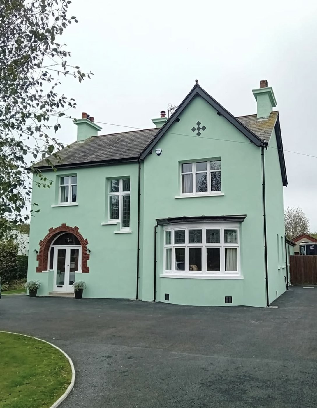 Detached house in a pale mint green finish with a red brick arch around the door